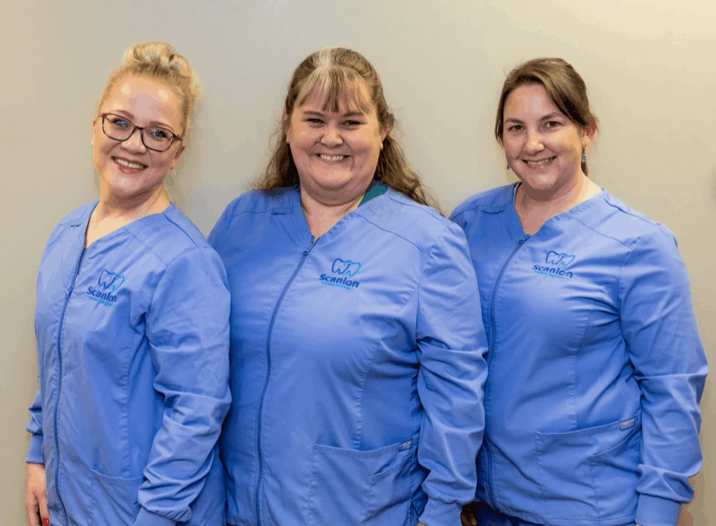 Dental professionals in blue scrubs posing together inside a dental office